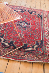 Vintage Bijar rug corner detail with cherry red field, navy border, ivory fringe, and wear.