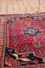 Hand-knotted vintage Bijar rug featuring a cherry red field, navy trefoil medallion, and ivory Herati motif.