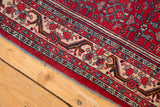 Corner of vintage Bijar rug, cherry red Herati field, ivory floral border, sky blue selvage.