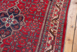 Detail view of a vintage Bijar rug's side, with red Herati field and complex ivory floral border.