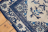Antique Peking rug corner: deep navy running-T border, ivory field, and visible end tatter.