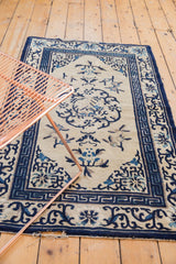 Antique Peking rug corner with Running-T border, ivory field, blue motifs, and edge tatter.