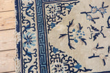 Antique Peking rug corner showing cobalt blue running-T border, ivory field, and edge tatter.