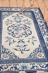 Antique Peking rug's ivory field with blue curvilinear motifs, Running-T border, and fringe.