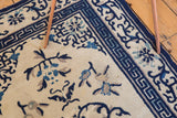 Ivory antique Peking rug with Running-T border and blue floral motifs, slight patina.