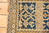 Close-up: Fringed edge and geometric flower border of antique Caucasian rug in navy and gold.