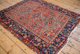 Corner of vintage Karaja rug: cherry red geometric field, navy border with rectilinear blossoms, fringe.