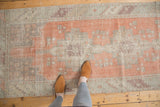 Distressed geometric pattern in bright terracotta, silver, beige, and aubergine tones.