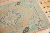 Distressed Oushak runner with faded peach, mint, aubergine scalloped medallion and decorative border.