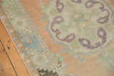 Distressed Oushak rug detail showing curvilinear aubergine motif, peach border, and low pile.