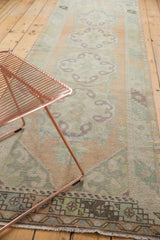 Distressed Oushak runner with softened peach, mint, and aubergine patterns and border.