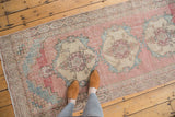Distressed vintage Oushak runner with faded pink, blue, and beige medallions, showing even wear.