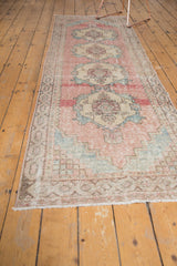 Distressed Oushak runner corner, showing faded pink, powder blue, checkered motif, and fringe.