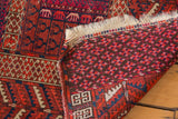Folded vintage Turkmen rug revealing dark cherry red motifs, ivory fringe, and hand-knotted back weave.