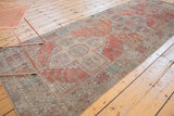 Dusty terra cotta distressed Oushak runner corner, hook-and-latch motif, moderate wear, and secured fringe.