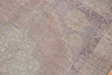 Distressed Oushak rug pile showing abrash, faint geometric patterns in mauve, lavender, beige.