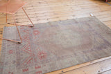 Distressed Oushak rug with worn pile, faint foundation, secured end, and faded terracotta motifs.