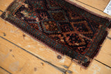 Antique Kurdish fragment corner showing textured pile, tattered fringe, and teal vine border.