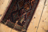 Close-up of antique Kurdish fragment rug with repeating diamond motifs, navy, teal, red, and aged edge.