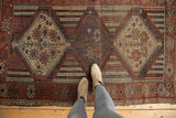 Antique Qashqai rug's geometric ivory medallion, red field, and light tatter to ends.