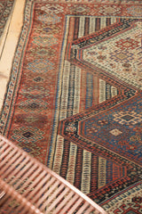 Antique Qashqai rug showing worn geometric patterns, with navy, red, and ivory striped channels.