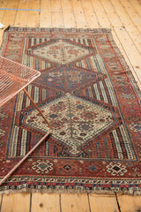 Antique Qashqai rug displaying intricate geometric patterns, visible wear, and tattered ends.