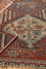 Detailed geometric patterns of an antique Qashqai rug, showcasing worn pile and tattered fringe.