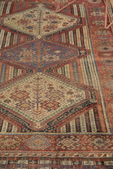 Antique Qashqai rug's intricate geometric patterns in ivory, navy, and reds, with visible wear to knot heads.