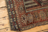 Antique Qashqai rug with tattered side edge and intricate geometric border patterns.