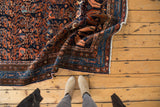 Folded vintage Hamadan rug revealing intricate navy, rust floral vinery and decorative border.