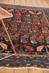 Corner of vintage Hamadan rug, with thick pile, serrated leaves, navy blue, dusty rust, and fringe.