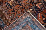 Folded corner of vintage Hamadan rug, highlighting intricate navy, rust, blush floral design.