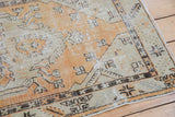 Corner detail of distressed Oushak rug, featuring faded tangerine and seafoam green serrated leaf border.