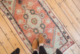 Distressed Oushak runner's splayed floral cross-sections in faded cherry red and seafoam green.