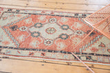 Vintage distressed Oushak runner with faded cherry red and seafoam floral designs.