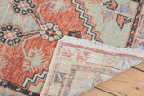 Distressed vintage Oushak rug corner revealing worn red and green pile, light fringe, and hand-knotted foundation.