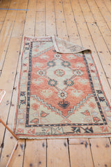 Distressed Oushak runner's textured pile, pale red floral patterns, and geometric border.