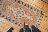 Distressed vintage Oushak runner with faded cinnabar red, ivory, and charcoal geometric patterns.