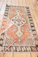 Distressed cinnabar red Oushak runner with geometric end finials, charcoal border, and fringe.