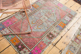 Distressed vintage Oushak rug pile with blush, tangerine, and pale blue geometric details.