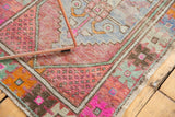 Distressed vintage Oushak rug corner with vibrant pink, orange, mint, and geometric seed motifs.