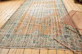 Distressed Oushak rug's worn texture, revealing faded apricot, burnt orange, beige, and mint blue.
