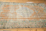 Distressed vintage Oushak carpet shows faded apricot, beige, mint green, and blue pile wear.