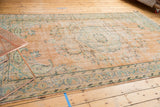 Distressed Oushak rug corner showcasing faded apricot, mint green paisley motifs and secure fringe.