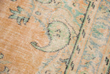 Worn texture of a distressed Oushak rug with apricot and mint green scrolling vinery.