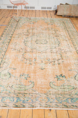 Distressed Oushak rug with faded apricot, mint green, and blue scrolling vinery.