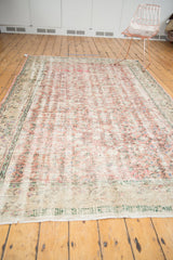 Distressed Oushak carpet with allover floral field, faded dusty rose, ivory, and mint green.