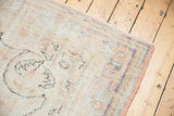 Distressed Oushak rug corner, revealing pile wear, pale blush, and faded inky blue border.