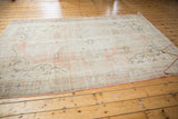 Distressed texture with faded dusty rose, pale blush, and charcoal tones on a vintage Oushak carpet.