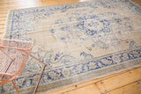 Distressed vintage Oushak carpet showing worn antique ivory field and faded royal blue floral motif.
